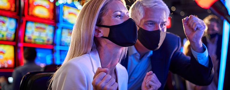 a couple with COVID masks excited at a slot machine playing casino games at carnival casino
